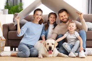 A happy mom and dad hold a cardboard representing a roof overhead, with the entire family, including their dog, smiling underneath, promoting HVAC membership monthly plan.