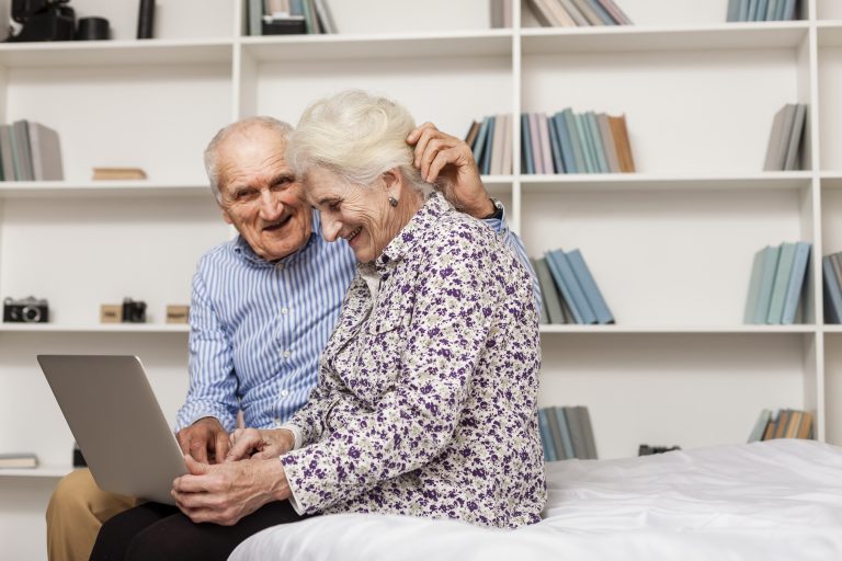 An older couple at home together, reading on a laptop