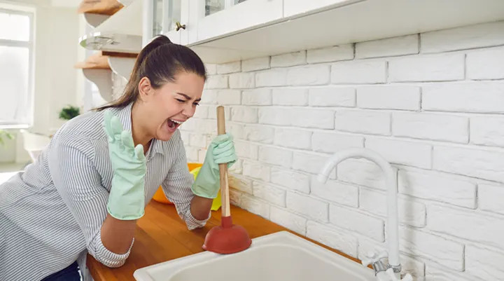 Frustrated Calgary homeowner plunging a clogged kitchen sink drain